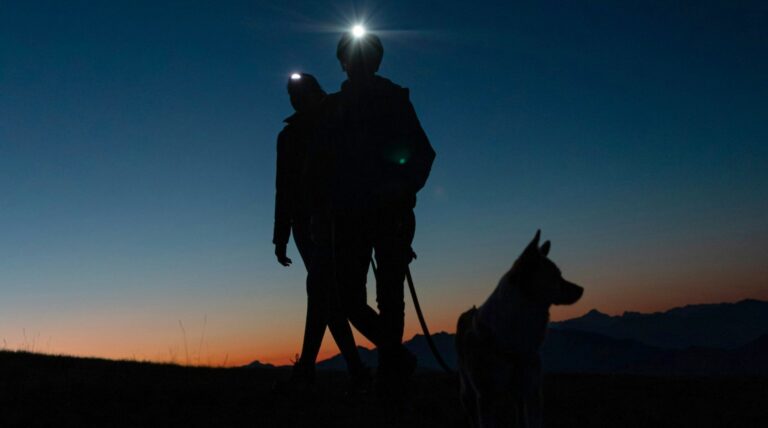 Zwei Menschen mit Stirnlampen und ein Hund als Silhouetten in der Abenddämmerung